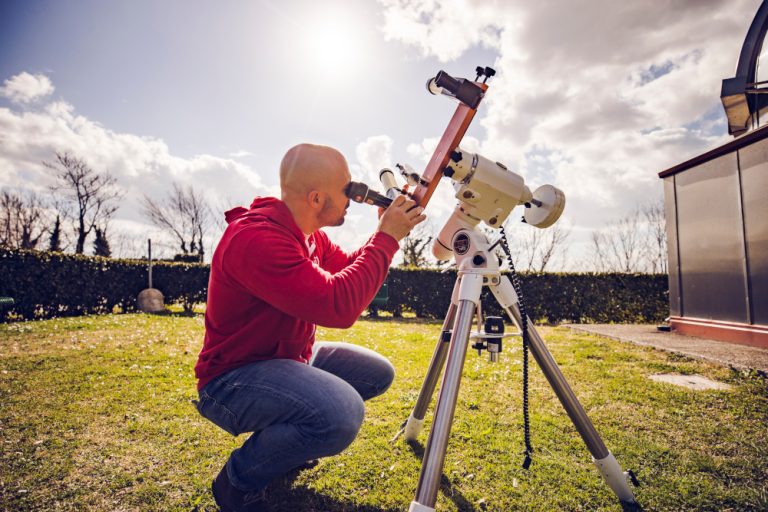 guida museale in felpa rossa che osserva il sole con un telescopio all'esterno di un osservatorio astronomico