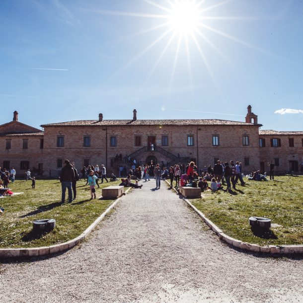 foto panoramica in cui si vede la villa del bal&igrave; con il sole sopra e la gente con i teli che fa picnic nel prato davanti all'edificio