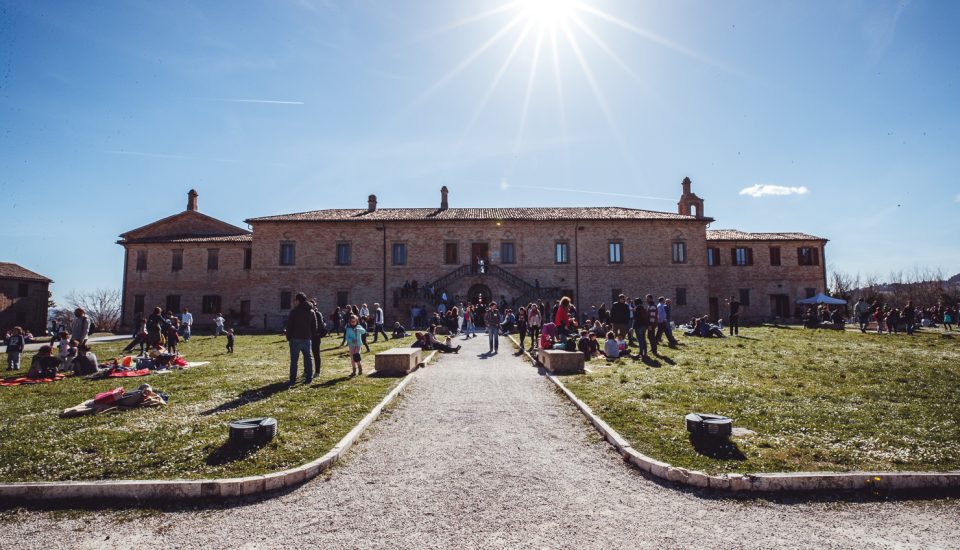 foto panoramica in cui si vede la villa del balì con il sole sopra e la gente con i teli che fa picnic nel prato davanti all'edificio